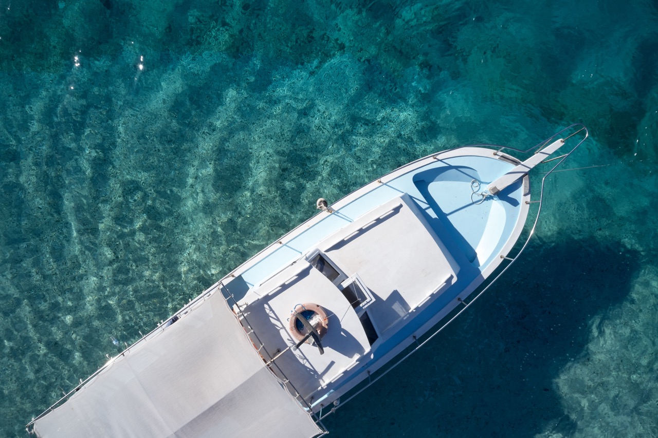 Top view of boat on clear turquoise water. Empty boat floating on crystal ocean water. View from above.